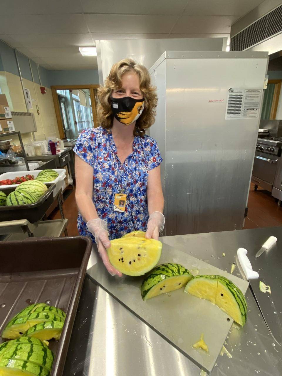 A school nutrition professional poses with a freshly cut yellow watermelon in the cafeteria kitchen.